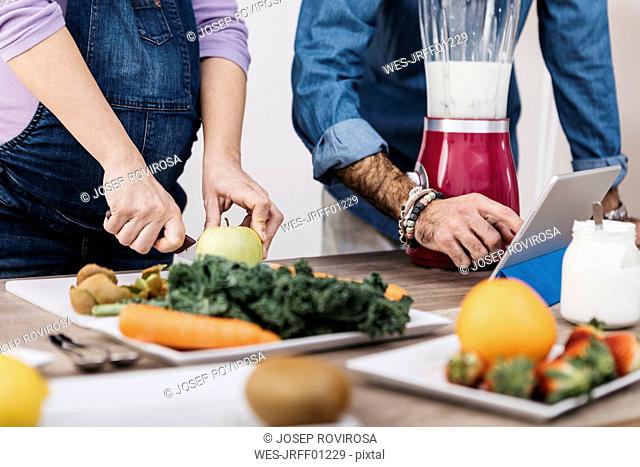 Hands of couple preparing fruits and using tablet for preparing smoothies