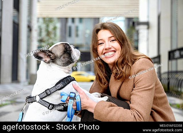 Happy woman stroking french bulldog at footpath