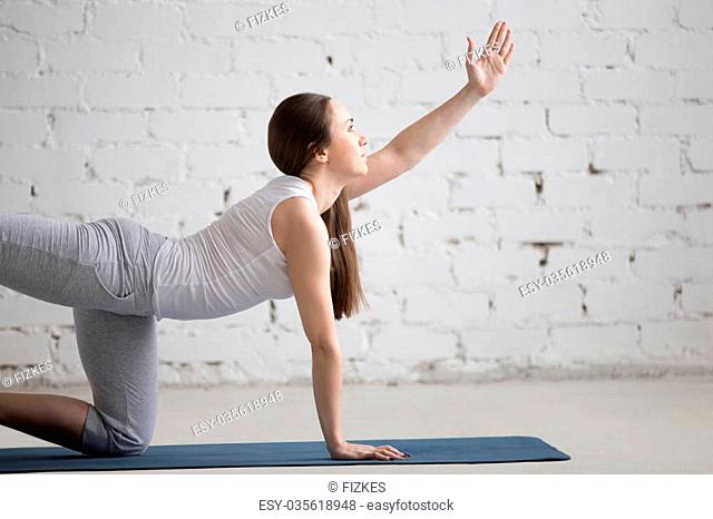 Portrait of attractive young woman working out indoors. Beautiful model doing exercises on blue mat in room with white walls