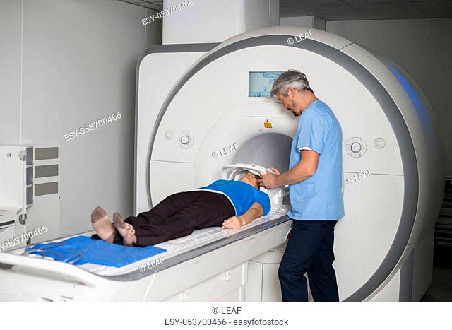 Male doctor fixing face mask to female patient lying MRI scan machine in hospital