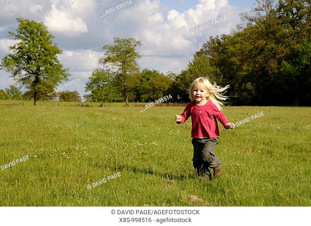 Stock photo of a blond haired 3 year old girl running in a field