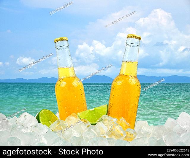 Close up two clear glass bottles of cold lager beer on ice cubes over background of summer sea and sky, low angle side view
