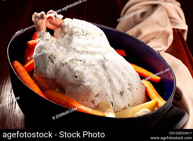 Whole raw chicken with fresh herbs and vegetables on wooden table. Salt crusted chicken
