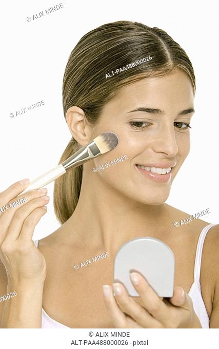 Woman applying blush, looking in hand mirror
