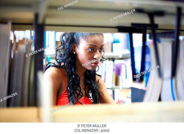 Young female college student searching library shelves