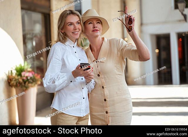 Stylish mature lady pointing at something in the distance to a smiling beautiful young female