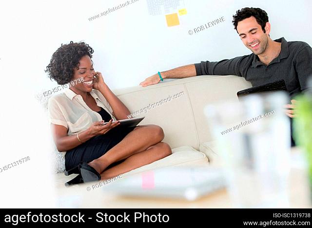 Office workers on sofa using digital tablets