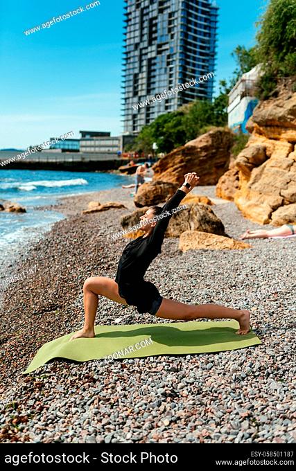 Young slim woman doing exercise for muscle on yoga mat outdoors at pebble beach by the sea