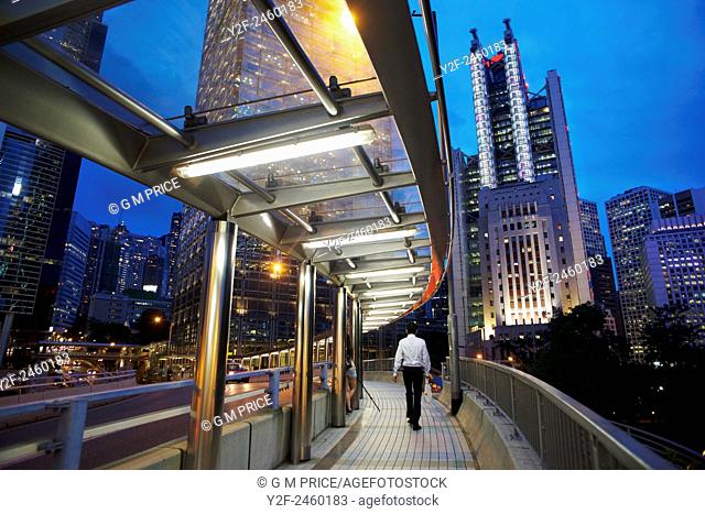 man on pedestrian walkway with Hong Kong Admiralty district skyline at dusk