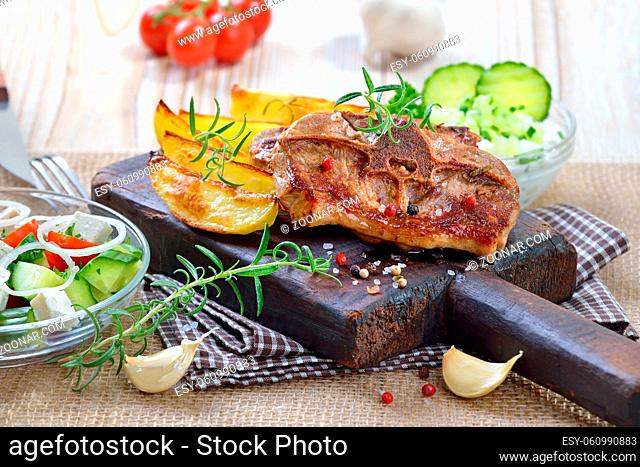 Gebratene Lammkoteletts mit Potato wedges, griechischem Bauernsalat und Tzatziki rustikal serviert - Fried lamb chops with potato wedges