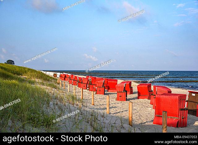 View over the dune and the deserted beach with red beach chairs in the early morning on the Darß