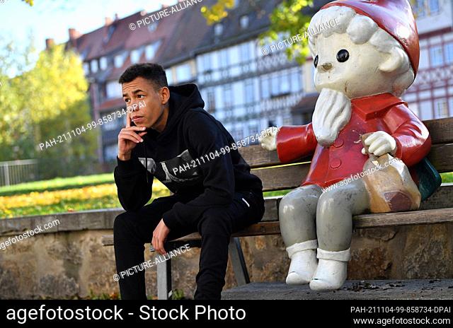 28 October 2021, Thuringia, Erfurt: The Erfurt rapper Michael Blanco Perez, MBP for short, sits on a bench behind the Krämerbrücke next to a Sandman figure