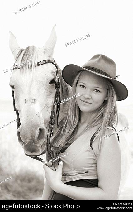Junge hübsche Frau mit langen blonden Haaren hält liebevolle Zwiesprache mit ihrem Pferd