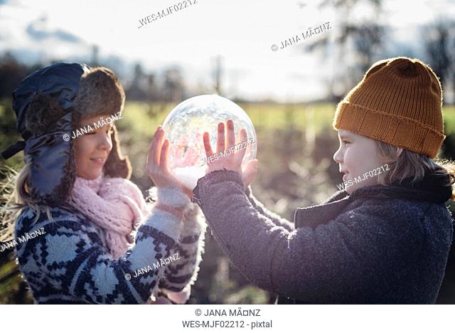 Brother and sister looking into crystal ball filled with snow, making a wish
