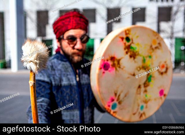 A close-up view of a traditional wood drum beater held by shaman in city surroundings. Bohemian fashioned guy stands in city street with music instrument