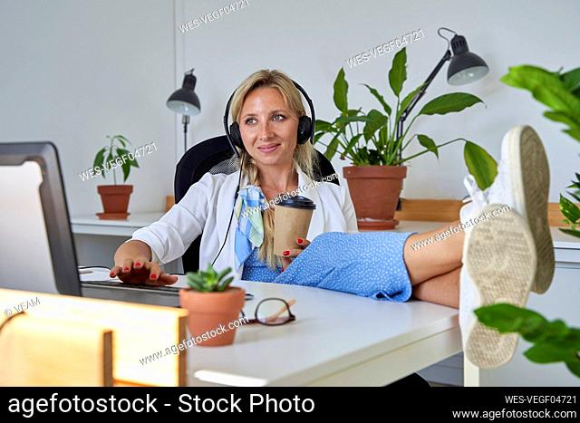 Female customer service representative having coffee while working on laptop at office