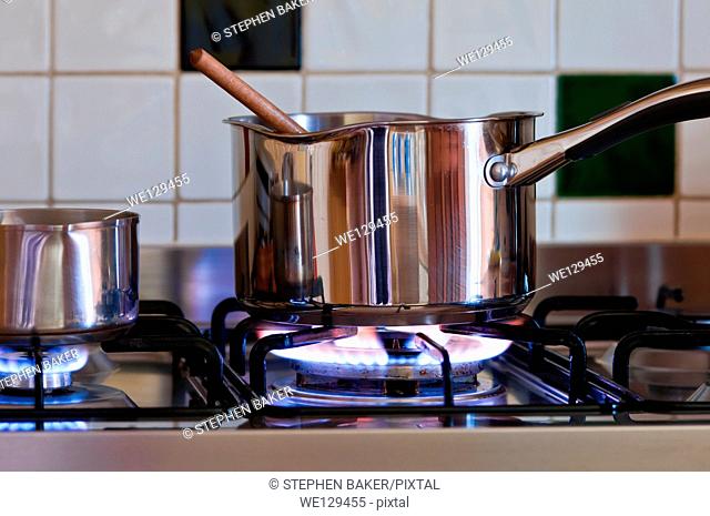 A saucepan with wooden spoon on gas hob having bought a sauce to simmer