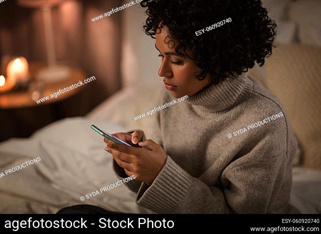 woman with smartphone sitting in bed at night