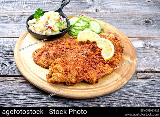 Traditional deep fried schnitzel with potato and cucumber salad offered as closeup on a rustic wooden board with copy space