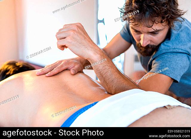 Physiotherapist massaging a muscular patient back with his elbow. Professional masseuse giving back massage to a sportsman
