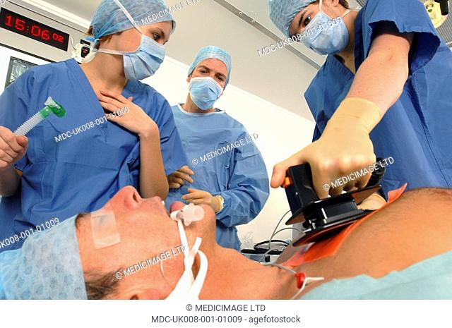Doctors using a defibrillator to resuscitate a male heart attack victim