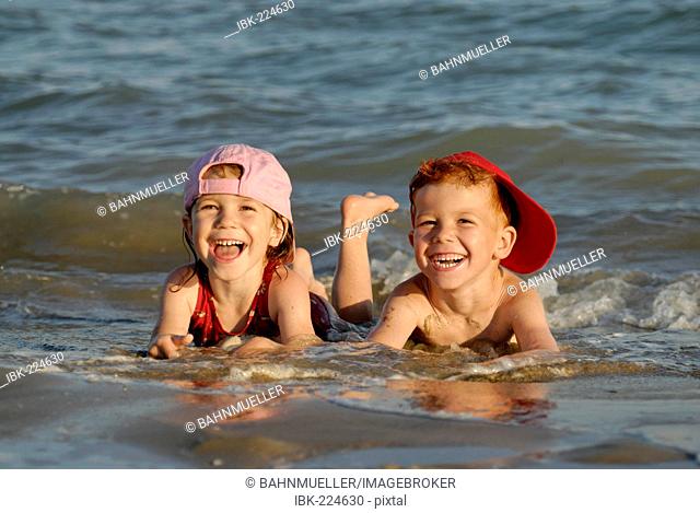 Two children are lying in the water at the beach and are having fun