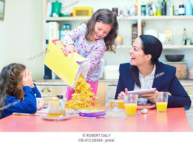 Playful girl pouring abundance of cereal onto breakfast table