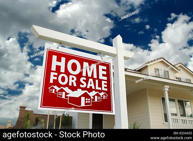 Red home for sale real estate sign and house against a blue sky