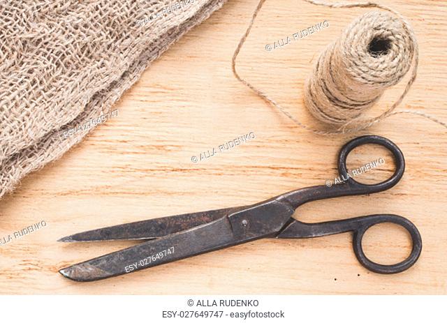 Old scissors, skein jute twine and burlap on a wooden background. Rustic style. Selective focus
