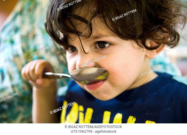 A boy trying to eat with a big spoon