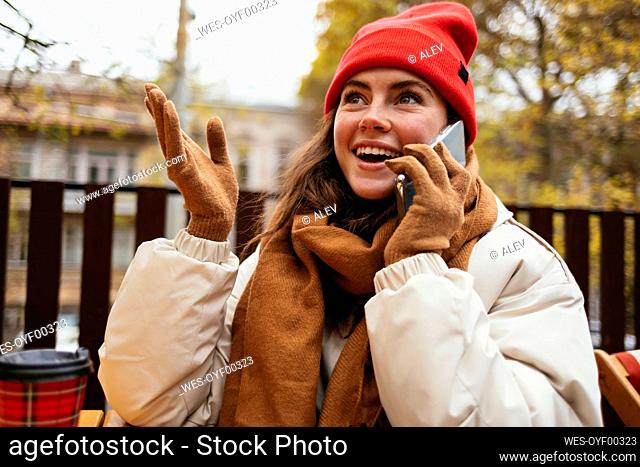 Smiling woman wearing knit hat gesturing while sitting at sidewalk cafe