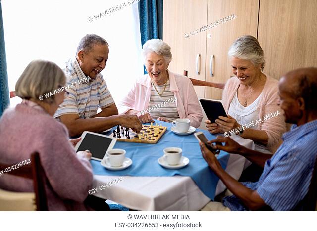 Senior friends playing chess and using technology at table