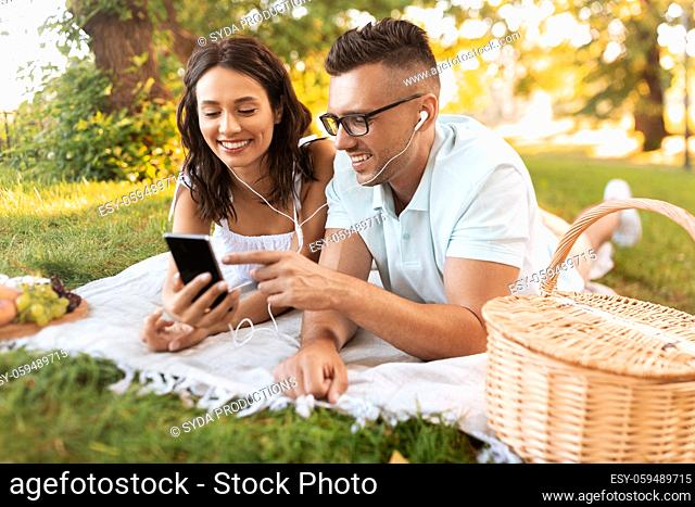couple with earphones and smartphone at picnic