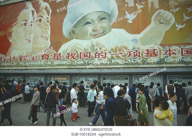 Busy street with pedestrains walking past family planning poster displayed overhead
