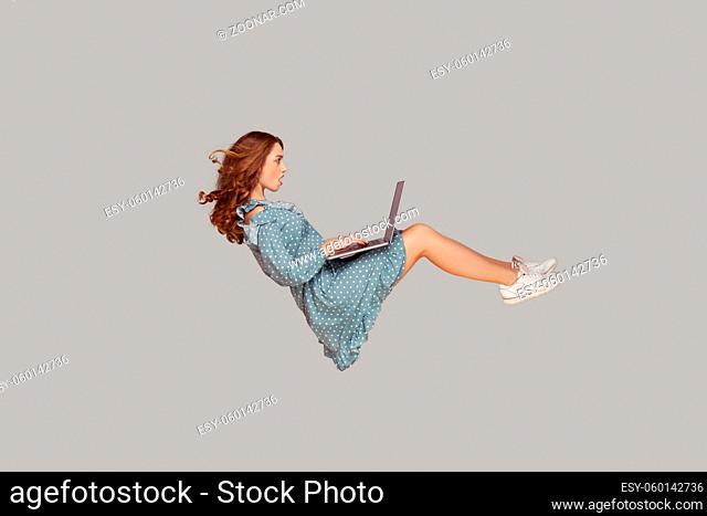 Hovering in air. Surprised girl ruffle dress levitating, looking at laptop screen shocked amazed, surfing web social networks while flying in mid-air