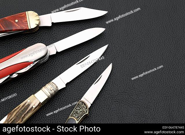 Close up photo of small folding knife on black leather background