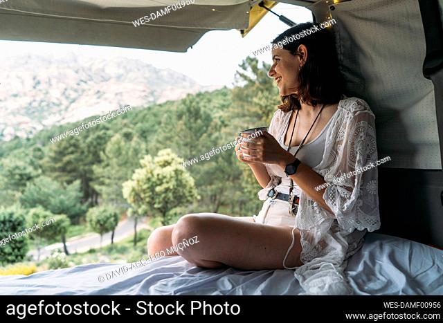 Smiling woman holding coffee cup sitting in van