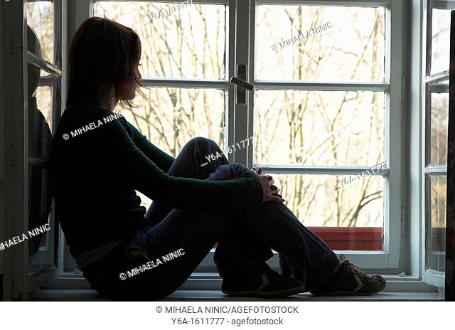 Woman silhouetted sitting on window ledge looking out of window