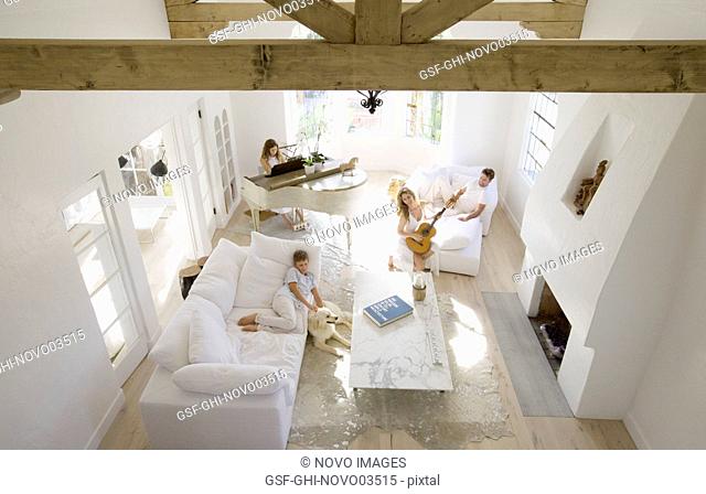 High Angle View of Family and Pet Dog in Living Room, Daughter Playing Piano, Mother Playing Guitar, Father and Son Relaxing on Sofas
