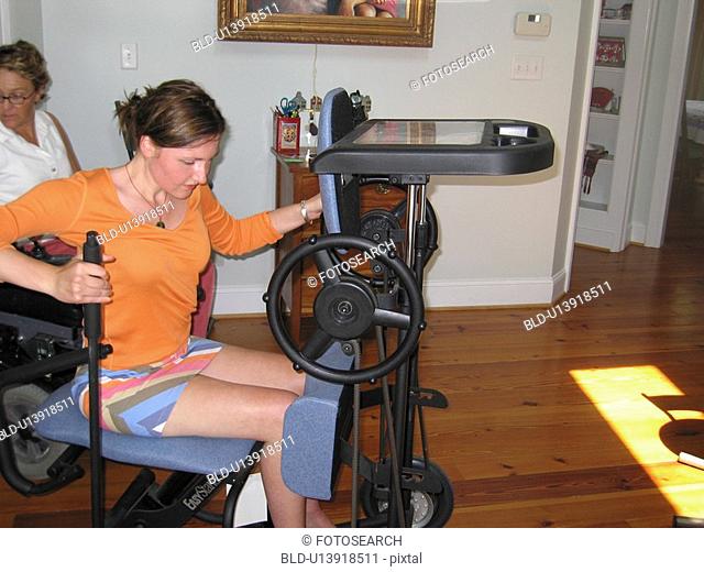 Young woman (muscular dystrophy) prepares to elevate herself on a stander for physical therapy