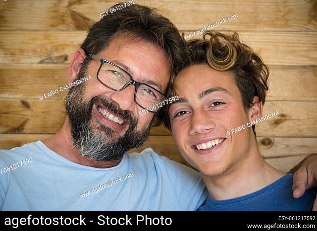 Father and son cheerful portrait with wood background - happy caucasian adult and young male family looking on camera