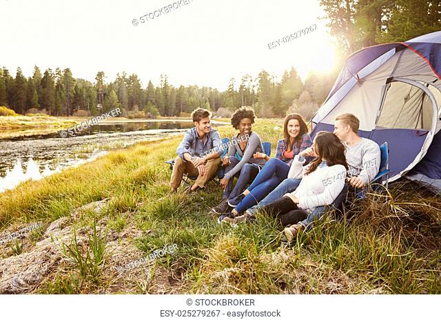 Friends on a camping trip relaxing by their tent near a lake