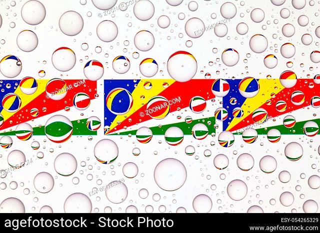 Flags of Seychelles behind a glass covered with raindrops. 3D illustration