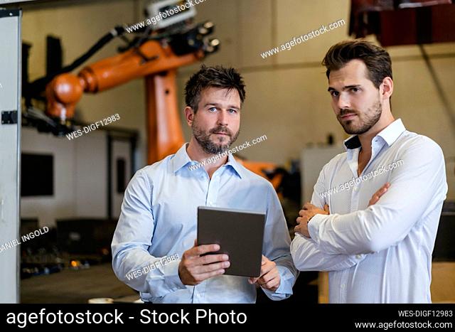 Empresarios confiados con tableta digital mientras están de pie en la fábrica
