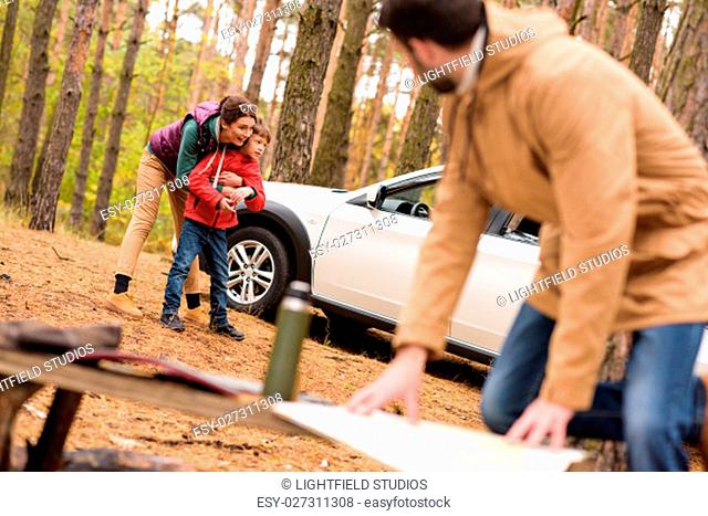 Young man looking at map and woman with boy standing near white car in autumn forest