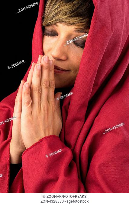 Schöne junge Frau im roten Umhang betet andächtig mit geschlossenen Augen und gefalteten Händen und lächelt geheimnisvoll