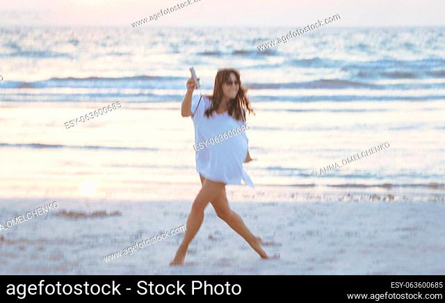 Photo in motion of a happy woman dancing on the beach. Having fun outdoors. Spending active summer holidays near the sea. Blur in motion