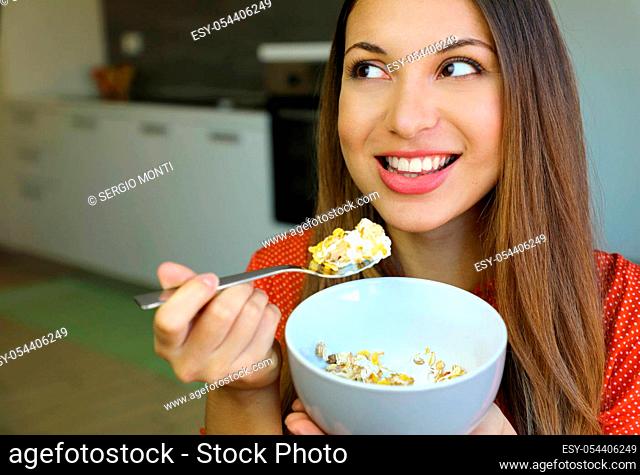 Close up of beautiful young woman eating skyr yogurt with cereal muesli fruit at home, looking to the side, focus on the model eyes, indoor picture
