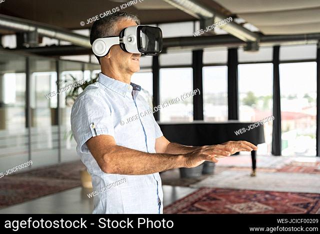 Happy businessman wearing virtual reality simulator standing in office