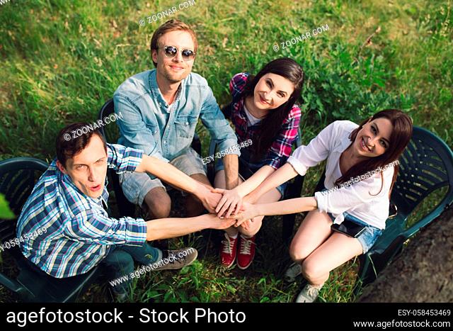 Top view of sweet friends spending time together outdoors. Lovely group of smiling people sitting together with their hands in middle looking up